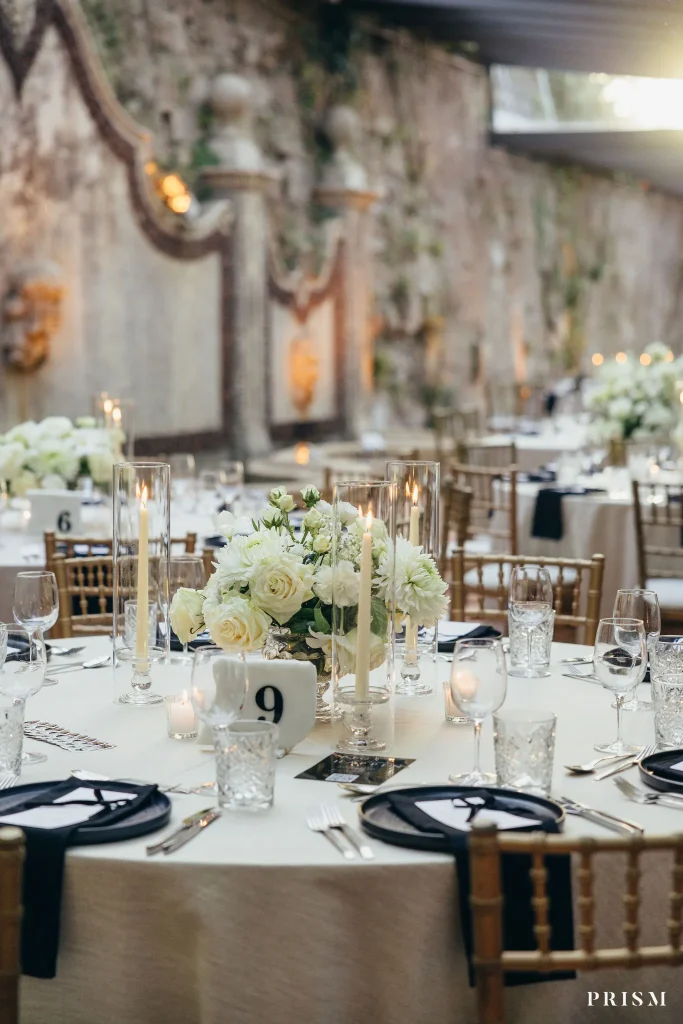 Sala de banquete com mesas redondas, centros de rosas brancas e velas